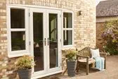 Cream uPVC French doors with side uPVC casement windows exterior view with wooden bench and blanket